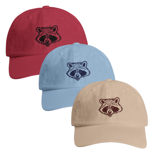 Three baseball caps in red, blue, and beige with raccoon face designs